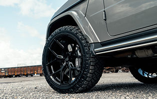 The Arabian Grey Mercedes G-63 AMG is outfitted with Custom Aftermarket Vossen HF-5 Wheels in Gloss Black finish. Shown here with an offroad Nitto Terra Grappler Tire for rugged terrain or overlanding.