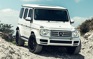 The White 2018 Mercedes G-550 is outfitted with Custom Vossen Hybrid Forged HF-7 Wheels in Gloss Black with an off-road tire for any terrain.